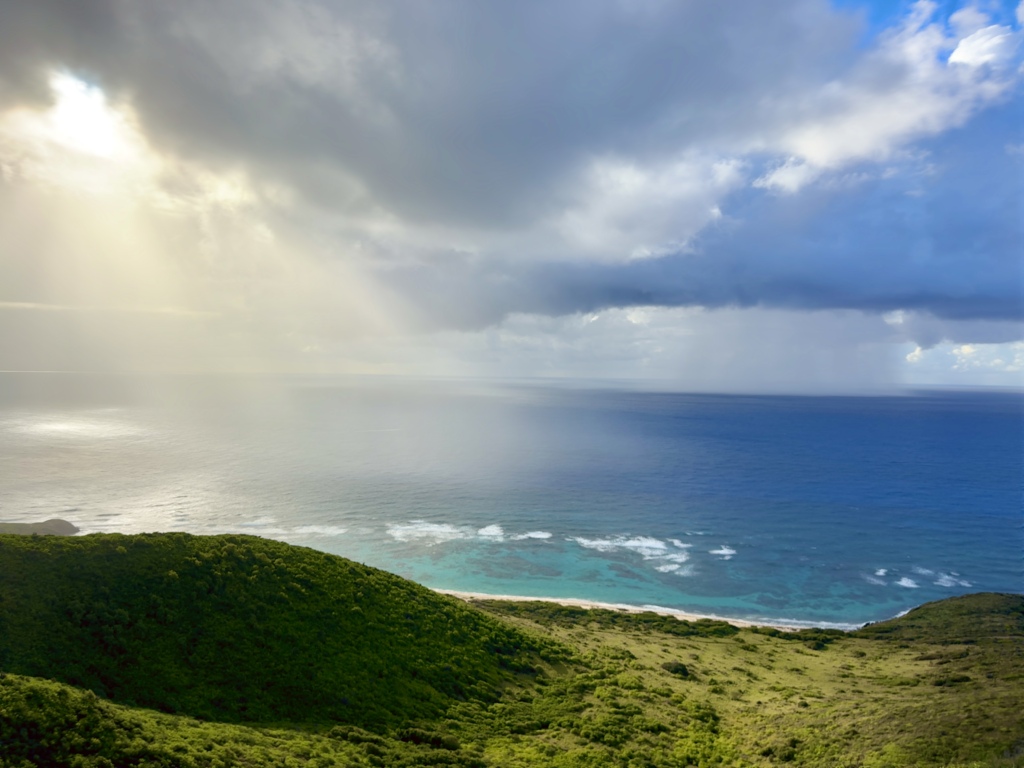 View from Goat Hill in St. Croix overlooking Jack Bay with turquoise water and sun rays breaking through clouds.