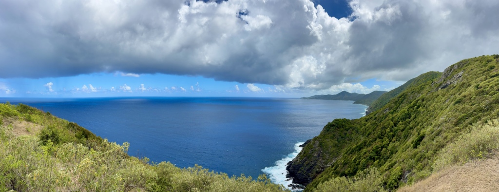 Panoramic view of St. Croix’s north shore with lush hills, rugged coastline, and deep blue Caribbean Sea under dramatic clouds.
