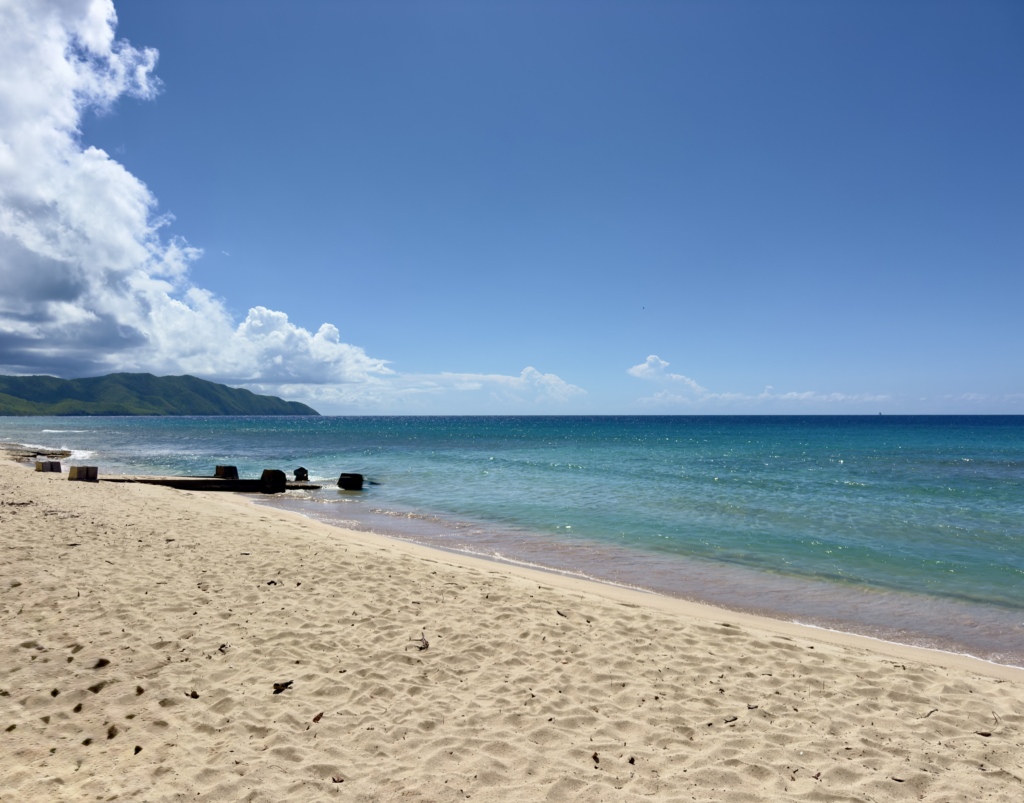 Sandy beach on St. Croix with calm turquoise water, a clear blue sky, and distant green hills along the coastline.