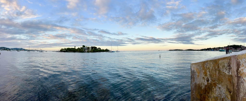 Panoramic view from the Christiansted Boardwalk at sunset, overlooking Christiansted Harbor with sailboats, Protestant Cay, calm Caribbean waters, and a colorful evening sky over St. Croix, U.S. Virgin Islands.