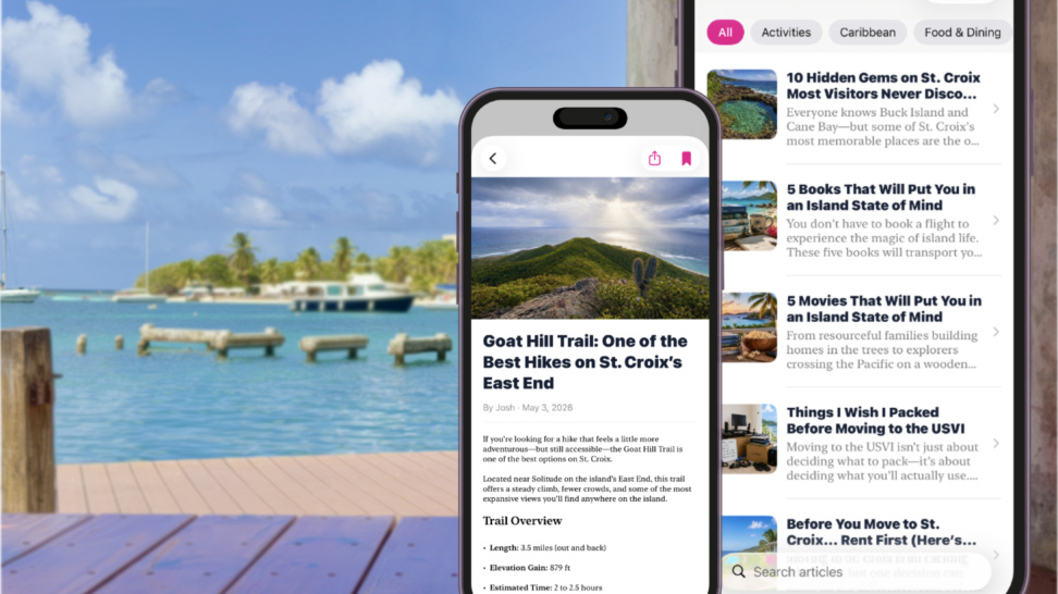 Composite image of the USVI Life iPhone app displayed over a scenic St. Croix waterfront, showcasing the app's home screen and a hiking article with Caribbean waters, boats, and tropical scenery in the background.